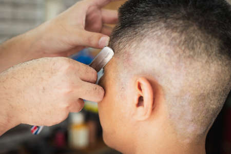 Asian young man being haircut with razor by professional barber in barbershop.の写真素材