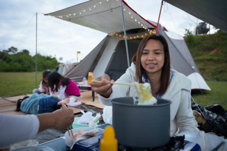 Asian woman eating shabu noodle outside the tent while camping with friend and family in the camping...
