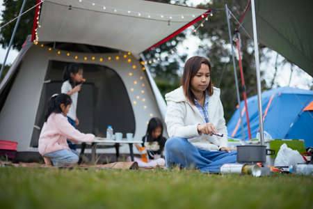 Asian mother cooking for family outside the tent while camping with family in the camping site with happiness. Family enjoy with nature and camping concept.の写真素材