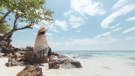 Asian woman sitting on the beach looking at the amazing sea and enjoying with beautiful nature in her vacation. Summer holidays and travel concept. Travelling in Thailand.の写真素材
