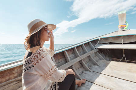 Traveling in Thailand. Asian woman sitting in the wooden longtail boat travel on the sea go to the amazing island and enjoying with beautiful sea and sky in her vacation.の写真素材