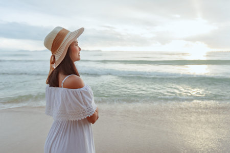 Asian woman wearing stylish hat and clothes looking to the ocean and enjoying beautiful Sunset on...
