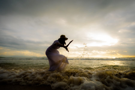Silhouette of asian woman playing water in the sea with wave on the beach and enjoying beautiful nature in the sunset time. Summer holidays and travel concept.の写真素材