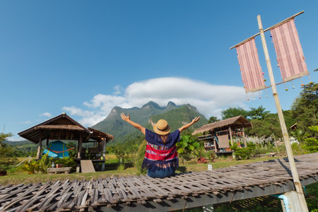 Backside of woman is sitting on bridge and enjoying with beautiful nature of mountain and sky while she travel on her vacation.の写真素材
