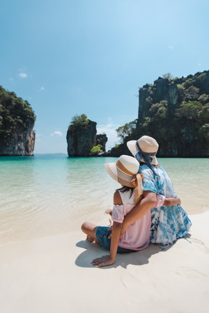 Asian mother and child girl sitting on the beach and enjoying with beautiful nature together in their vacation. Summer holidays and family travel concept. Travelling in Thailand.の写真素材
