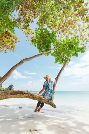 Asian woman sitting on the tree and enjoying with beautiful sea nature in her vacation. Summer holidays and family travel concept. Travelling in Thailand.の写真素材