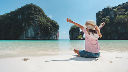 Backside of asian child girl wearing hat sitting on the beach and enjoying with beautiful nature in her vacation with family. Family trip and Thailand travel concept.の写真素材
