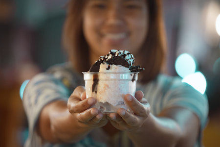 Asian woman holding delicious ice cream dessert in a cup in night market. Thai famous gourmet street...