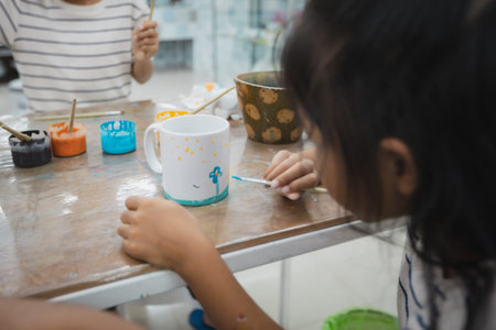 Asian child girl and friends are concentrating to paint on ceramic glass with oil color together...