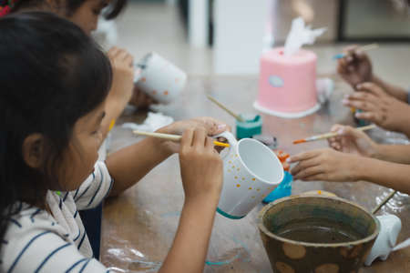Asian child girl and friends are concentrating to paint on ceramic glass with oil color together with fun. Kids arts and crafts creative activity class in school.の写真素材