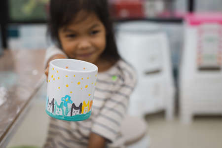 Asian child girl showing her own work after finished paint on ceramic glass with oil color. Kids arts and crafts creative activity class in school.の写真素材