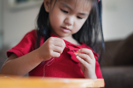 Close up hand of asian child girl is threading beads onto a string with intention and fun in home.の写真素材
