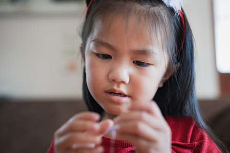 Close up hand of asian child girl is threading beads onto a string with intention and fun in home.の写真素材