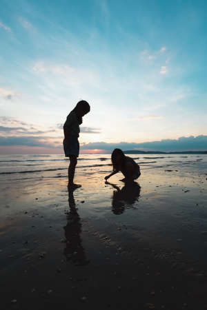 Silhouette of two asian child girls playing on the beach together at the sunset time with beautiful sea and sky. Family enjoy with nature concept.の写真素材