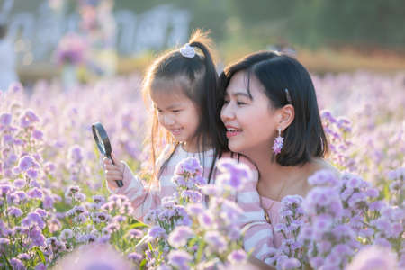 Cute asian child girl and her mother enjoying with beautiful flower together and little girl holding magnifier looking on flower with fun and curiously in the flower garden.の写真素材