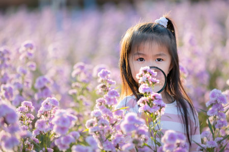 Cute asian little child girl holding magnifier looking on flower with curiously and enjoying with beautiful flower in the flower garden.の写真素材