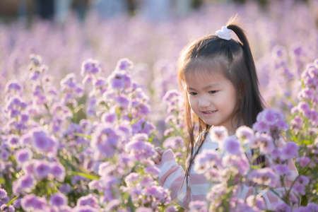 Cute asian little child girl holding magnifier looking on flower with curiously and enjoying with beautiful flower in the flower garden.の写真素材