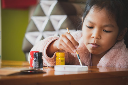 Close up asian child girl painting on plastic bottle with watercolor to recycle to be a flower pot. Kids arts and crafts creative activity in home during quarantine due to Covid 19 pandemic.の写真素材