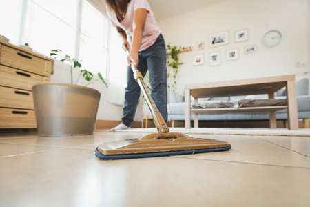 Asian woman cleaning and mopping the floor with a microfiber wet mop pad in the living room. Woman doing chores at home. Housekeeping concept.の写真素材