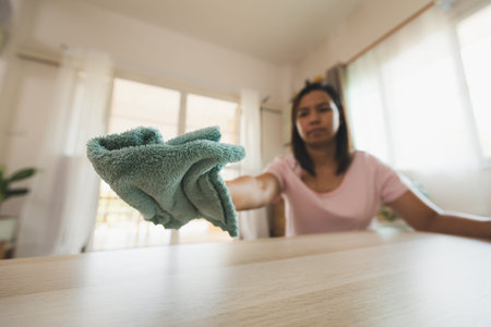 Woman cleaning and wiping the table with microfiber cloth in the living room. Woman doing chores at...