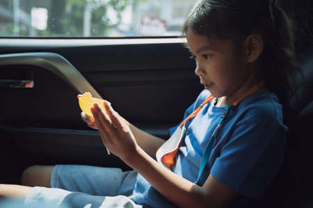 Asian child girl is playing her toy in the car while traveling to school. Childhood and family lifestyles in car concept.の写真素材
