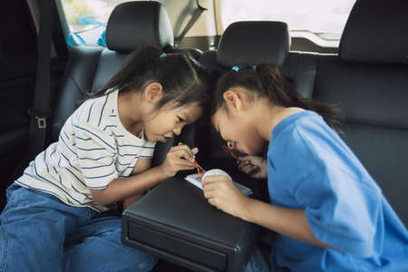 Two asian child girls eating dessert together while traveling in the car. Childhood and family lifestyles in car concept.の写真素材
