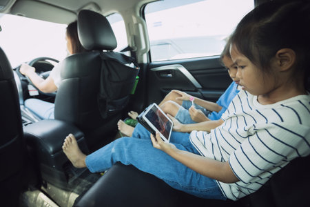 Two asian child girls sitting on backseat and watching cartoon in tablet together while traveling in...