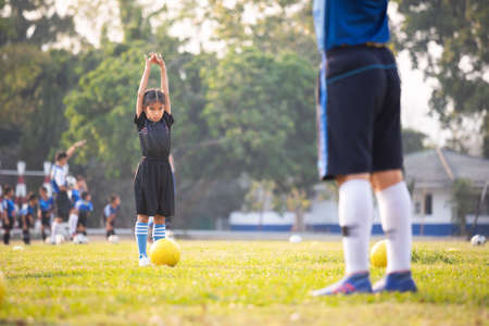 Asian child girl exercise warm up before play soccer with coach and friend. Kid sport recreation concept.の写真素材