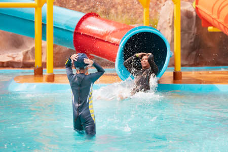Backside of asian child girl is looking at her father slide down on water slide in a water park with excited at the summer time.の写真素材
