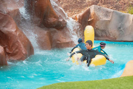 Asian father and two childs having fun to sit in the rubber ring floating on the water together in a water park at the summer time.の写真素材
