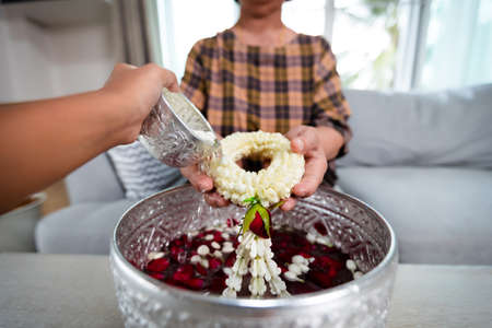 Point of view of child pouring water on hands of elder senior or respected grandparents who holding jasmine garland on hand for celebrate Songkran in new year water festival.の写真素材