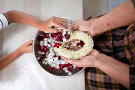 Top view of child pouring water on hands of elder senior or respected grandparents who holding jasmine garland on hand for celebrate Songkran in new year water festival.の写真素材