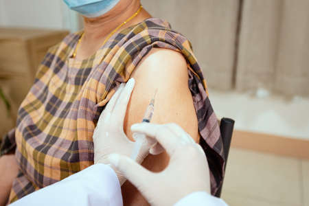 Close up on doctor is injecting vaccination on senior woman arm. Adult patient wearing protective face mask for protect pandemic. Health care and medical concept.の写真素材