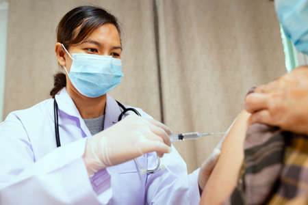 Doctor injecting vaccination on senior woman arm. Doctor and adult patient wearing protective face mask for protect  pandemic. Health care and medical concept.の写真素材