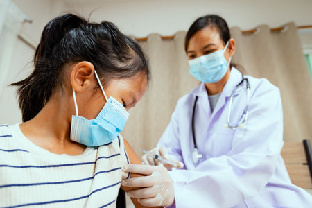 Doctor injecting vaccination on asian child girl arm. Doctor and child patient wearing protective face mask for protect virus  pandemic. Health care and medical concept.の写真素材