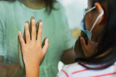 Social distancing among the family. Close up on hands of mother and daughter on a window plane. Stay at home during quarantine due to virus pandemic.の写真素材