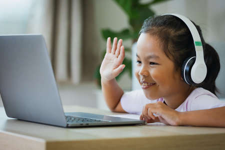 Asian child girl student wear headphone study online with teacher by video call. Child is homeschooling with computer laptop during quarantine due to  pandemic.の写真素材