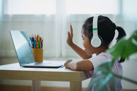Asian child girl student wear headphone study online with teacher by video call. Child is homeschooling with computer laptop during quarantine due to pandemic.の写真素材