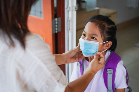 Asian mother helping her daughter wearing medical mask before go outside for protection  virus outbreak situation as new normal lifestyle. Healthcare and Social Distance concept.の写真素材