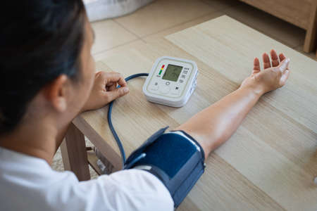 Asian young woman is checking blood pressure and heart rate with digital pressure gauge by herself at home. Health and Medical concept.の写真素材