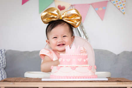 Portrait of cute asian baby girl celebrating her first birthday with pink princess cake with happiness.の写真素材