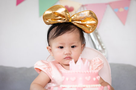 Portrait of cute asian baby girl celebrating her first birthday with pink princess cake with happiness.の写真素材