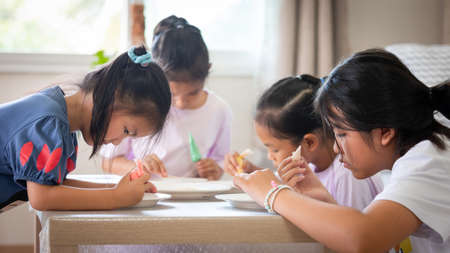 Asian child girl and friends are decorating cookies for party together with fun. DIY homemade kid art and craft concept.の写真素材