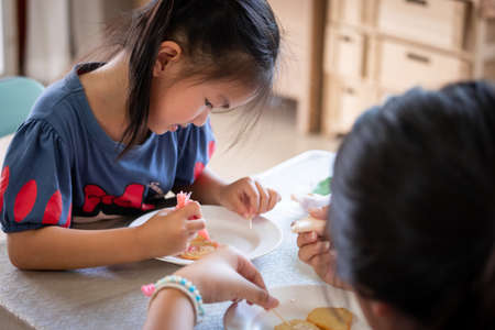 Asian child girl and friends are decorating cookies for party together with fun. DIY homemade kid art and craft concept.の写真素材
