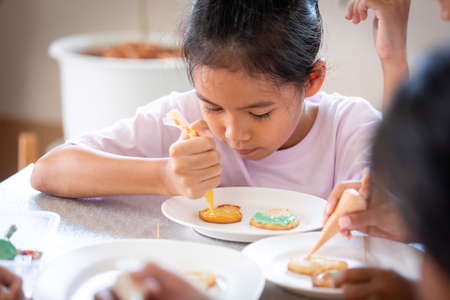 Close up asian child girl squeezing icing cream to decorate cookies with friend with fun. DIY homemade kid art and craft concept.の写真素材