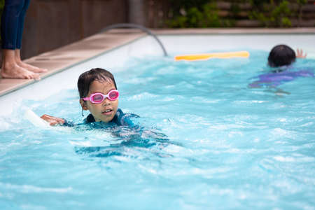 Asian child girl playing water and swimming in the swimming pool with her friend with fun. Summer activity and childhood lifestyle concept.の写真素材