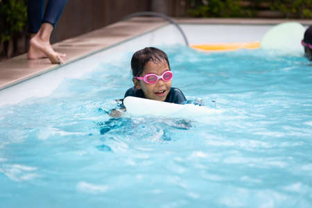 Asian child girl playing water and swimming in the swimming pool with her friend with fun. Summer activity and childhood lifestyle concept.の写真素材