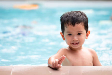 Portrait of asian little boy looking at camera and smiling while playing water in the swimming pool. Summer activity and childhood lifestyle concept.の写真素材