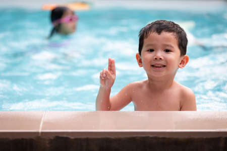 Portrait of asian little boy looking at camera and smiling while playing water in the swimming pool. Summer activity and childhood lifestyle concept.の写真素材
