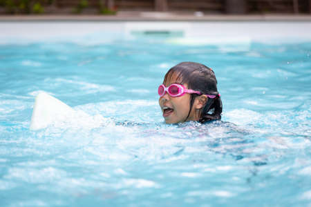 Asian child girl playing water and swimming in the swimming pool with her friend with fun. Summer activity and childhood lifestyle concept.の写真素材